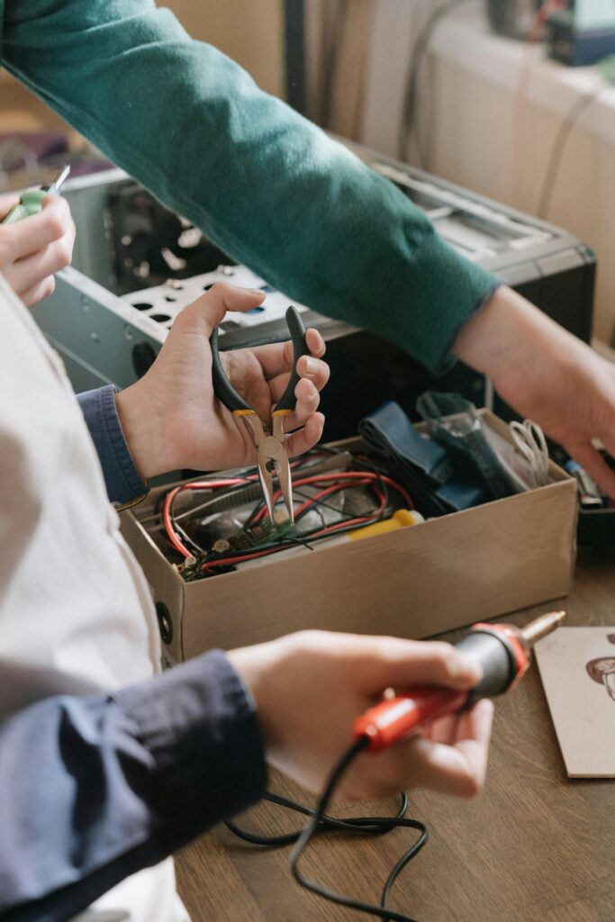Close-up of hands repairing electronic device using soldering iron and pliers.