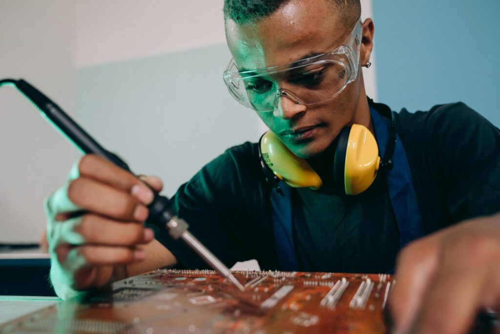 Young male engineer working on circuit board soldering with precision and focus.
